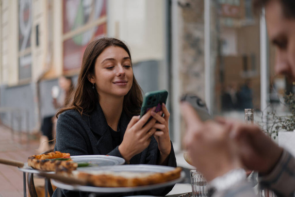 Sitting in restaurant, texting on smartphones. Boyfriend, girlfriend on date browsing mobile phone - Foto, imagen