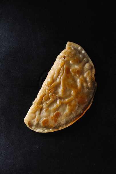 A levitating half of a fried cheburek with leaking hot stretchy cheese. On a black background with a slight gradient. Fast food. - Photo, Image