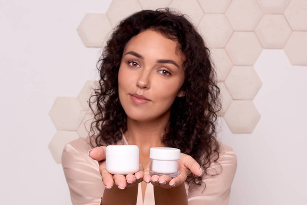 body care cosmetics. woman holding two white jars with cream in hands in front of face. selective focus on hands - Photo, Image