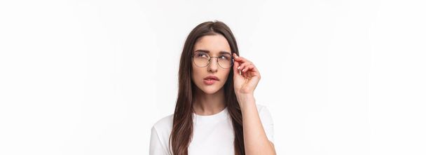 Κοντινό πλάνο πορτρέτο της έξυπνης και στοχαστική όμορφη νεαρή κοπέλα σε γυαλιά, σκέψης, squinting ύποπτες και δάγκωμα χείλη κοιτάζω προς τα πάνω, ενώ μελετώντας κάτι, έχουν ενδιαφέρουσα ιδέα, λευκό φόντο. - Φωτογραφία, εικόνα