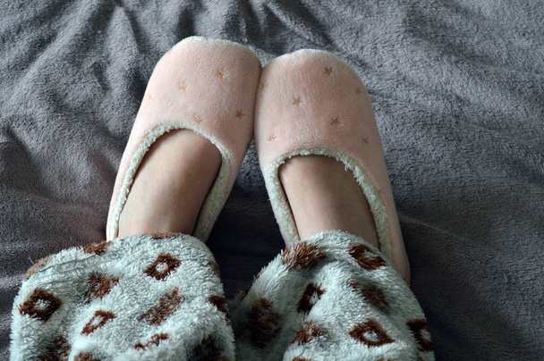 Girl on the bed in warm home slippers and rhombus print pajamas, home comfort and coziness - Fotó, kép