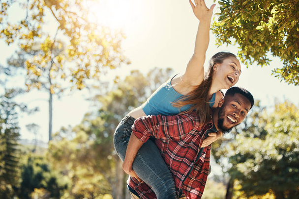 Divertido, casal e diversão piggyback com um homem e mulher se divertindo na natureza durante o verão. Aventura, casal feliz e pessoas inter-raciais em um jardim verde ou ambiente natural com felicidade. - Foto, Imagem