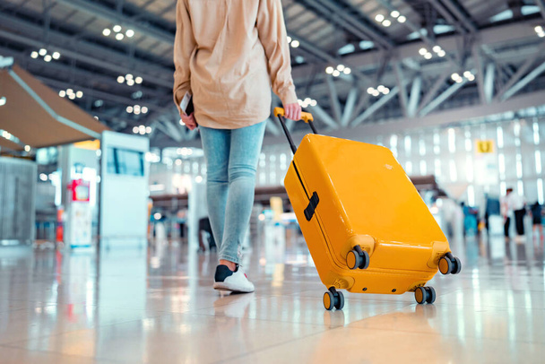 Νεαρή γυναίκα ταξιδιώτης επιβάτης περπατώντας με κίτρινη βαλίτσα στο σύγχρονο Αεροσταθμό Αεροδρομίου, Πίσω όψη της γυναίκας στο δρόμο της προς την πύλη επιβίβασης, έτοιμη για ταξίδι ή ταξίδι διακοπών - Φωτογραφία, εικόνα