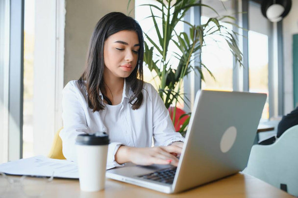 Estudante menina alegre estudando on-line no café, usando laptop e fones de ouvido, espaço vazio. - Foto, Imagem