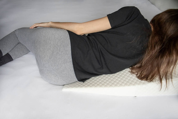 Dziewczyna leży na łóżku na poduszce w kształcie klina na refluks żołądka z pianką żelu - Zdjęcie, obraz