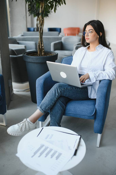 Young charming female freelancer using laptop computer for distance job while sitting in modern coffee shop interior, beautiful Caucasian woman working on net-book during morning breakfast in cafe bar. - Foto, imagen