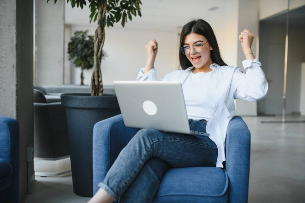 Girl rejoices in winning having raised her hands up sitting in front of laptop.Girl sitting in cafe, watches online sports match on computer.Woman blogger enjoys lot of views of her videos on Internet - Foto, Bild
