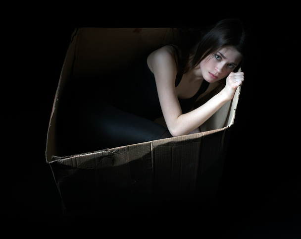 Concept of homeless. Upset girl in cardboard box - Foto, afbeelding