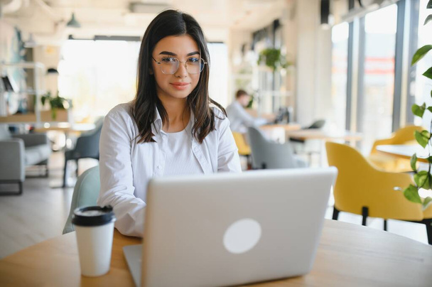 Freelance, business and e-commerce concept. Creative enthusiastic female journalist writing new article, typing on laptop, smiling, write-down project ideas, sit cafe, drink coffee working remote. - Photo, Image