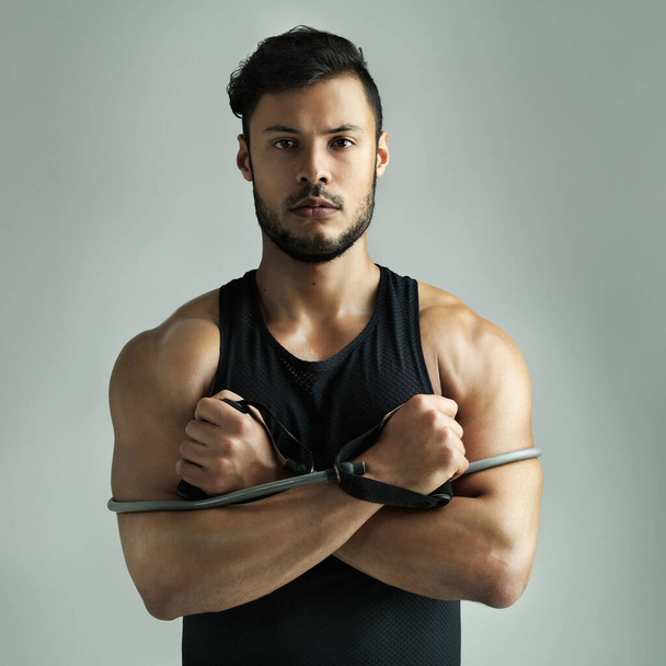 Ready for some resistance training. Studio shot of a young man working out with a resistance band against a gray background - Фото, зображення