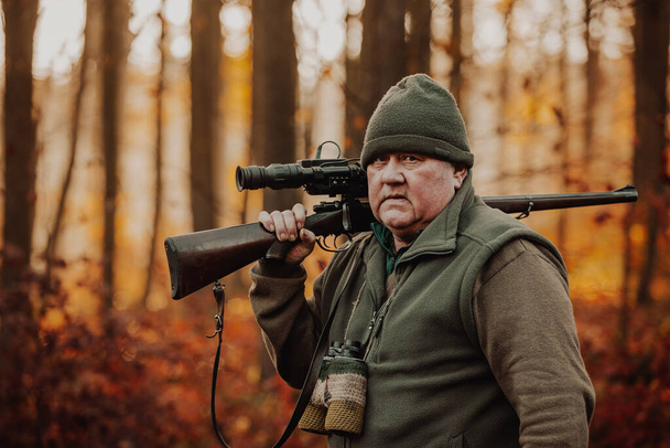 Portret van een jager of boswachter met geweer of geweer in een bos die op zoek is naar of jaagt op een wild, jachtperiode, herfstseizoen, jacht- en mensenconcept - Foto, afbeelding