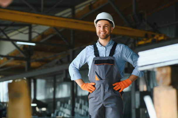 Portrait of factory worker in protective uniform and hardhat standing by industrial machine at production line. People working in industry. - Foto, immagini