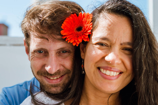 retrato de homem argentino com barba e mulher brasileira, adultos latinos, em casa eles estão olhando para a câmera com uma flor no ouvido e sorrindo - Foto, Imagem