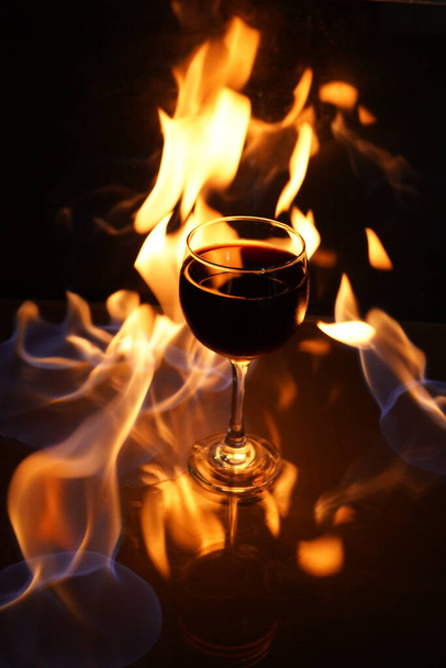 glass of red wine on the table with fire in the background fine art - Foto, Imagen