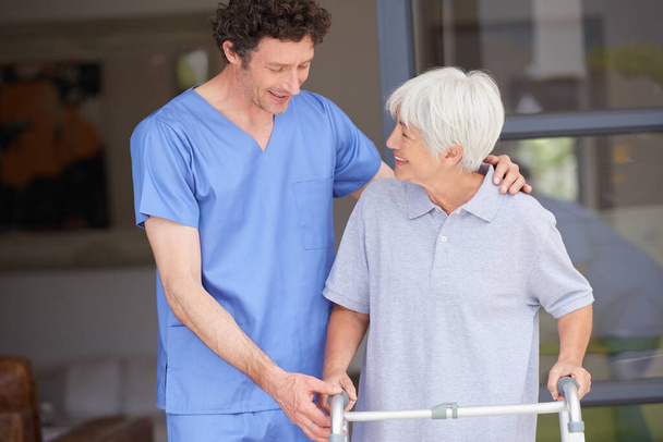 Dobrze sobie radzi ze starszymi pacjentami. mężczyzna lekarz pomaga jego starszy pacjent whos za pomocą walker dla wsparcia - Zdjęcie, obraz