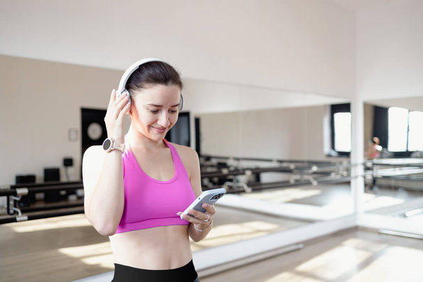 Active young caucasian sporty athletic fitness trainer instructor woman using smartphone, listening to music in gym. Workout sport concept.  - Zdjęcie, obraz