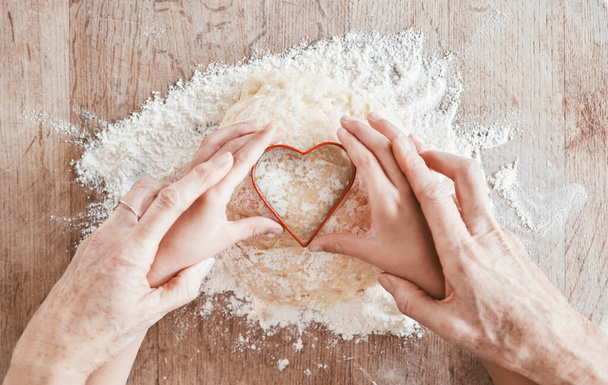 .Hands, baking and heart shape with a girl and grandmother learning how to bake in the kitchen of their home together. Family, children and food with a woman and granddaughter bonder over cooking - Photo, Image