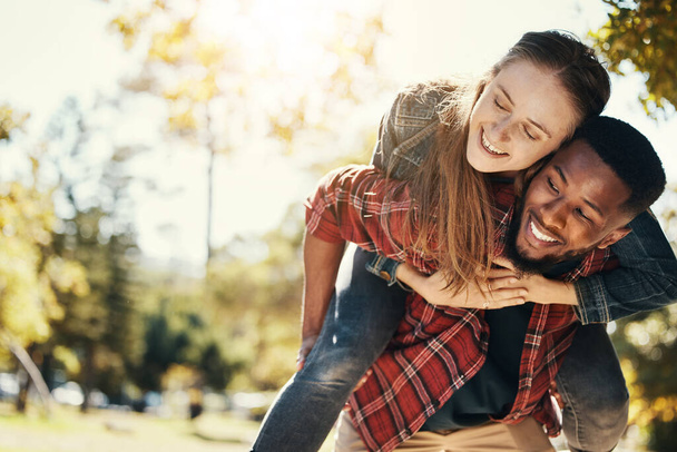 Love, care and interracial couple with piggyback in a park for support, adventure and happy with mockup and bokeh. Hug, smile and black man and woman on an outdoor date in nature with space in summer. - Photo, Image