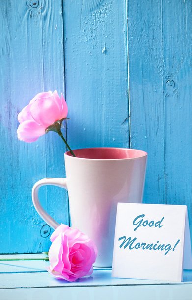 Tazza con rose rosa su sfondo di legno blu con testo buongiorno
 - Foto, immagini