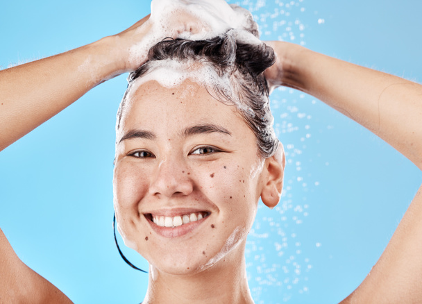 Woman, shampoo and shower in studio portrait with hair care, cleaning and smile by blue background. Model, hair and wellness with foam, soap or water for self care, cosmetics or beauty with happiness. - Foto, Imagem