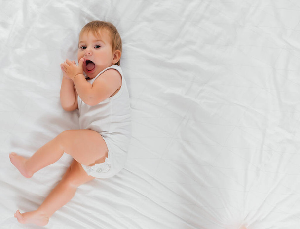 a child on a white bed in the morning. Textiles and bed linen for children. A newborn baby has woken up or is going to bed. - Foto, Bild