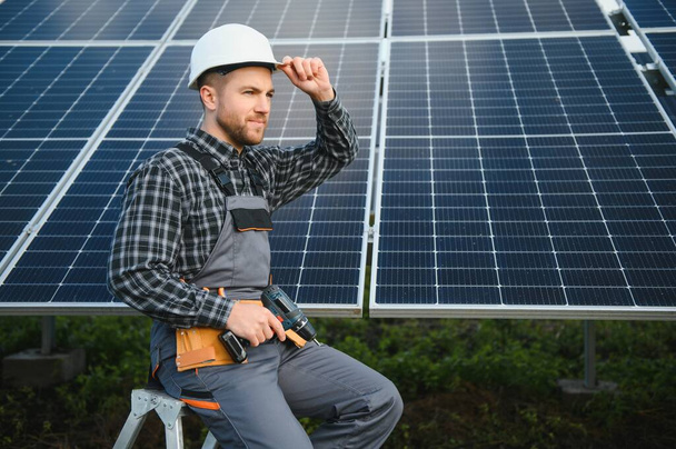 Portrait of smiling confident engineer technician with electrical screwdriver, standing in front of unfinished high exterior solar panel photo voltaic system. - Φωτογραφία, εικόνα