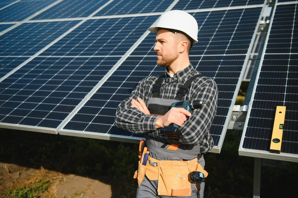 Male worker in uniform outdoors with solar batteries at sunny day - 写真・画像