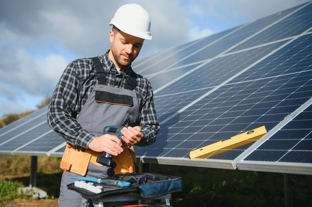 Portrait of smiling confident engineer technician with electrical screwdriver, standing in front of unfinished high exterior solar panel photo voltaic system. - Photo, image