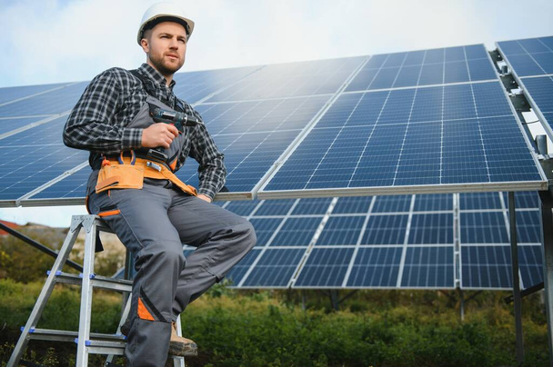 Male worker in uniform outdoors with solar batteries at sunny day - Photo, image