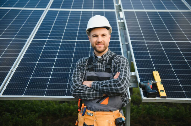 A handyman standing on the rooftop with solar panels and smiling at the camera - Photo, image