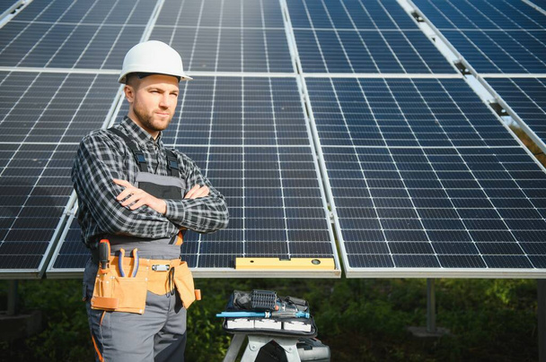 Male worker in uniform outdoors with solar batteries at sunny day - Foto, afbeelding