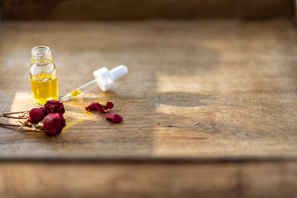 Essential oil in a small glass bottle with dried pink roses in bud on a wood background. Selective focus and copy space for text. Natural cosmetic products. - Foto, imagen
