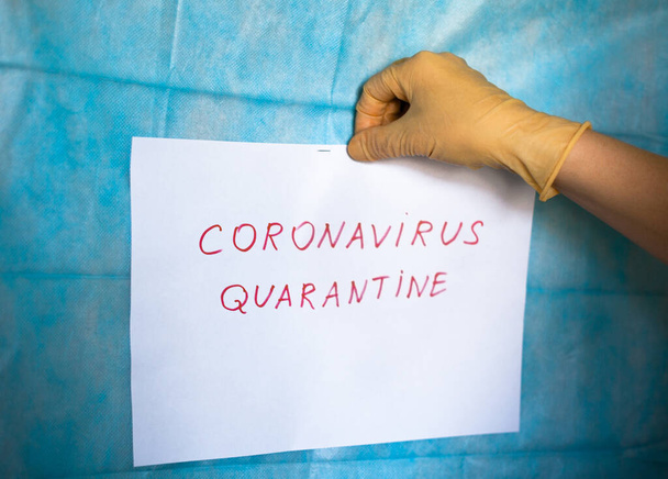 Rękawica medyczna wisząca na białym papierze z ręcznie napisanym napisem Coronavirus Quarantine. Kwarantanna, aby zapobiec rozprzestrzenianiu się infekcji. Epidemia koronawirusu (Covid-19). - Zdjęcie, obraz