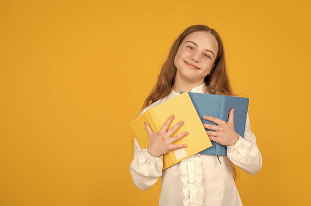 веселый ребенок держать школьную книгу на желтом фоне с копировальным пространством, образование. - Фото, изображение