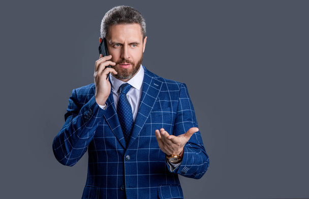 serious businessman talk on phone isolated on grey background. businessman having phone talk in studio. photo of businessman talk on phone. businessman talk on phone in suit. - Photo, Image