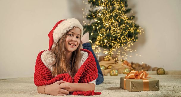 merry christmas. cheerful teen girl wear santa hat. kid in knitted scarf. child at home decorated for xmas. childhood happiness. winter holiday and vacation. prepare and celebration. happy new year. - Fotografie, Obrázek