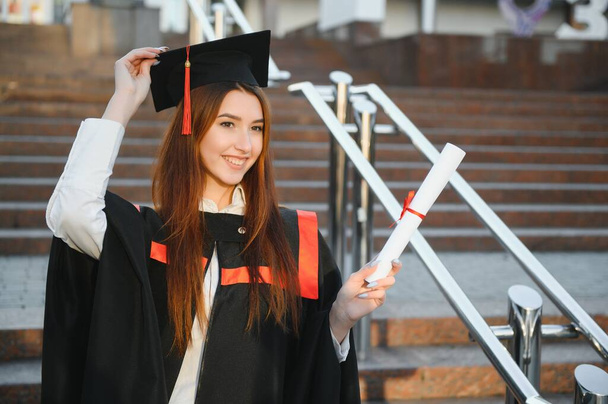 Happy graduation day for a young woman very beautiful with graduation cap smile large in front of the Camera posing while holding her diploma. - 写真・画像