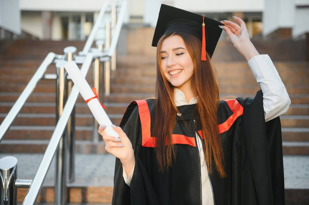 Happy graduation day for a young woman very beautiful with graduation cap smile large in front of the Camera posing while holding her diploma. - Fotografie, Obrázek
