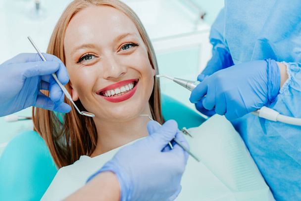Attractive young woman smilling with natural white teeth in dental clinic. Hands doctor dentist with medical tools. Healthy teeth concept - Photo, Image