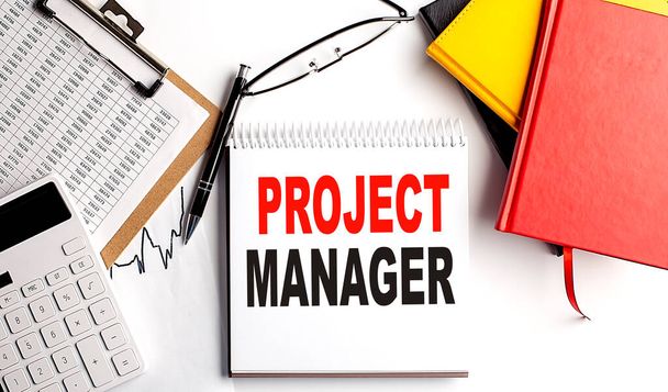 PROJECT MANAGER text on a notebook with clipboard and calculator on white background - Photo, Image