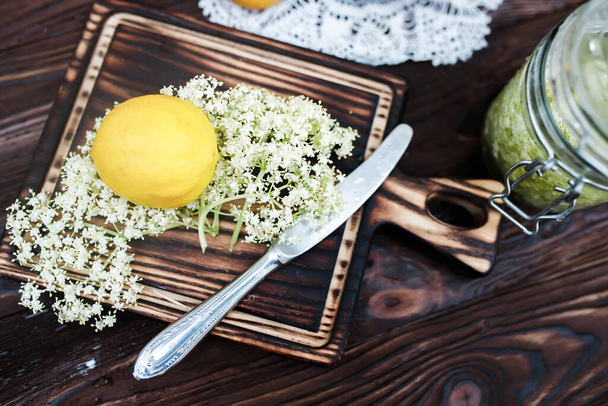 Molienda de limón y saúco negro en una tabla de cortar para hacer una bebida a base de hierbas o medicina para la curación en casa de jarabe de flores de saúco. - Foto, imagen