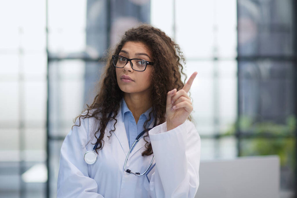 Portrait of an attractive young female doctor in a white coat points her finger - Фото, зображення