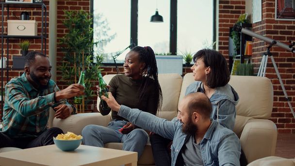 Multiethnische groep mensen die toast maken met bierflessen, conversatie en hechting hebben. Lachen en praten over vriendschap, ontspannen en plezier hebben in de hangplek. - Foto, afbeelding