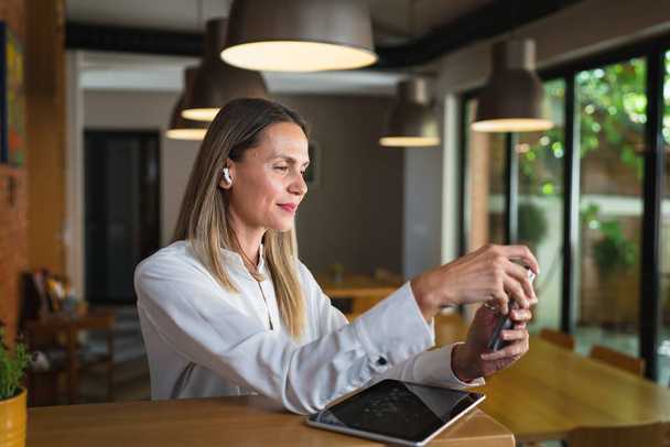 Μια γυναίκα ενήλικας μεσήλικας καυκάσιος γυναίκα στέκεται στη δουλειά χαρούμενος χαμόγελο αυτοπεποίθηση φορούν λευκό πουκάμισο μέση μέχρι αντίγραφο χώρο μπροστά προβολή πορτρέτο χρησιμοποιώντας το κινητό τηλέφωνο κάνοντας μια κλήση ή να στείλετε sms αυτοπεποίθηση - Φωτογραφία, εικόνα