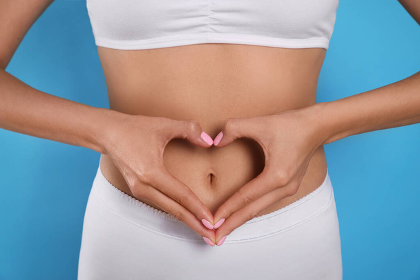 Woman in underwear making heart with hands on her belly against light blue background, closeup. Healthy stomach - Fotó, kép
