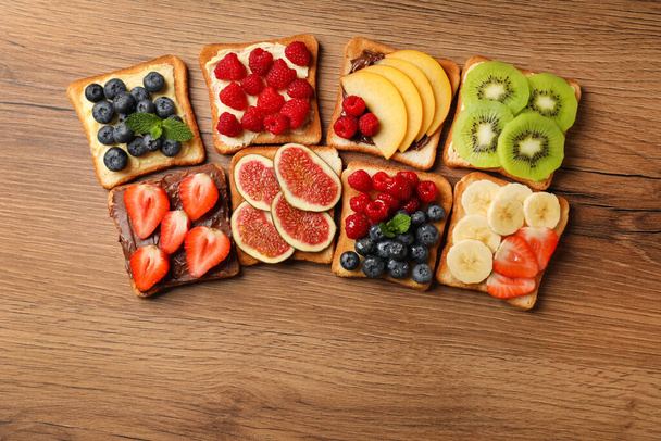 Leckere Toasts mit verschiedenen Brotaufstrichen und Früchten auf Holztisch, flach gelegt - Foto, Bild