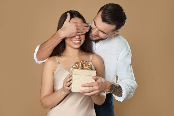 Man presenting gift to his girlfriend on beige background - Фото, зображення