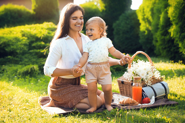 Mother with her baby daughter having picnic in garden on sunny day - Photo, image