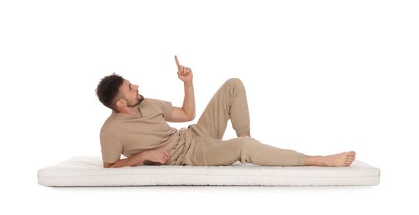 Man lying on soft mattress and pointing upwards against white background - Photo, Image