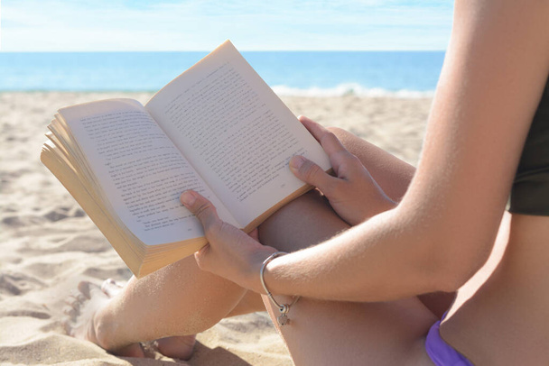 Woman reading book on sandy beach near sea, closeup - Fotó, kép